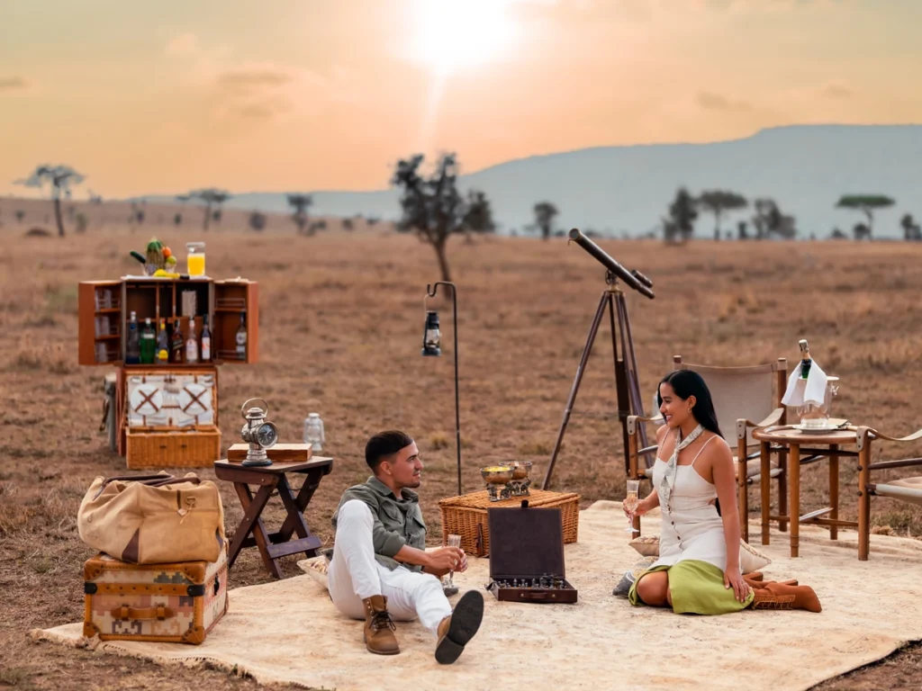 Couple Enjoying Sundowners: A couple toasting drinks during a romantic sundowner, with the Serengeti sunset in the background.